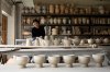 Eine Frau sitzt in einem Atelier umgeben von vielen Keramikarbeiten.
