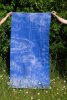 Ein blaues Textilobjekt wird auf einer Wiese mit zwei Händen getragen und zur Schau gestellt.